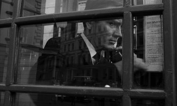 Movie still from “Repulsion” (1965), directed by Roman Polanski – A black and white photo of a man smoking a cigarette in front of a building; Close Up shot, Low angle