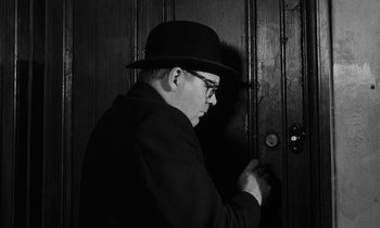 Movie still from “Repulsion” (1965), directed by Roman Polanski – A man in a hat and glasses standing in front of a door; Close Up shot, Low angle