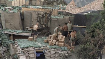 Movie still from “Restrepo” (2010), directed by Tim Hetherington – A group of men standing next to a pile of sandbags; Wide shot, High angle