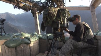 Movie still from “Restrepo” (2010), directed by Tim Hetherington – A man sitting on top of a hill looking through a telescope; Wide shot, High angle