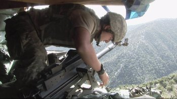 Movie still from “Restrepo” (2010), directed by Tim Hetherington – A man in fatigues and a helmet standing in a helicopter; Wide shot, Low angle