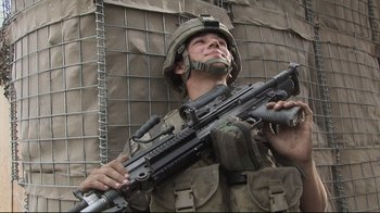 Movie still from “Restrepo” (2010), directed by Tim Hetherington – A soldier holding a rifle in front of a wire wall; Medium shot, Low angle