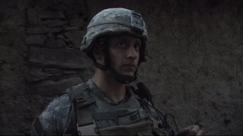 Movie still from “Restrepo” (2010), directed by Tim Hetherington – A man in a military uniform is standing in front of a stone wall; Close Up shot, Over the shoulder angle