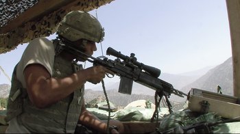 Movie still from “Restrepo” (2010), directed by Tim Hetherington – A man in fatigues holding a rifle in a field; Medium shot, Low angle