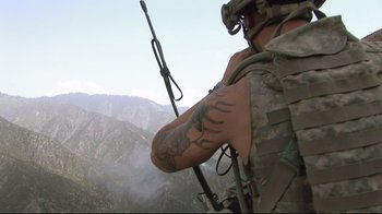 Movie still from “Restrepo” (2010), directed by Tim Hetherington – A man in fatigues holding a rifle on top of a mountain; Wide shot, Low angle