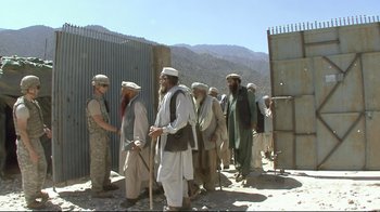 Movie still from “Restrepo” (2010), directed by Tim Hetherington – A group of men standing next to each other on a street; Wide shot, Over the shoulder angle