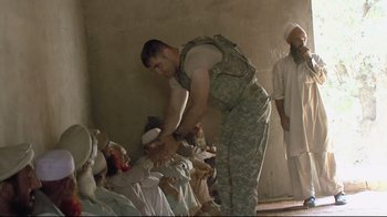 Movie still from “Restrepo” (2010), directed by Tim Hetherington – A man in fatigues is helping a group of people; Medium shot, High angle