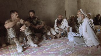 Movie still from “Restrepo” (2010), directed by Tim Hetherington – A group of men sitting on the ground in a room; Medium shot, Over the shoulder angle
