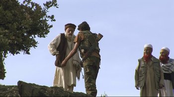 Movie still from “Restrepo” (2010), directed by Tim Hetherington – A man standing next to a man in a military uniform; Wide shot, Low angle