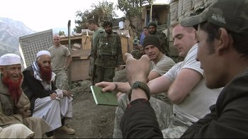 Movie still from “Restrepo” (2010), directed by Tim Hetherington – A group of men standing next to each other on a dirt field; Medium shot, Over the shoulder angle