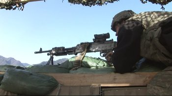 Movie still from “Restrepo” (2010), directed by Tim Hetherington – A man with a rifle sitting on a bench; Wide shot, Low angle