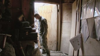 Movie still from “Restrepo” (2010), directed by Tim Hetherington – A man standing in front of an open door; Medium shot, Low angle