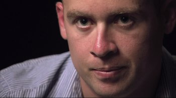 Movie still from “Restrepo” (2010), directed by Tim Hetherington – A man's face in a blue shirt; Extreme Close Up shot, Low angle