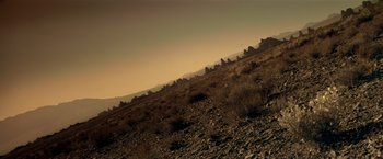 Movie still from “Revenge” (1990), directed by Tony Scott – A view of a mountain range from the side of a hill; Extreme Wide shot, Low angle