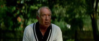 Movie still from “Revenge” (1990), directed by Tony Scott – An older man in a white sweater looking off into the distance; Close Up shot, Low angle