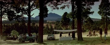 Movie still from “Revenge” (1990), directed by Tony Scott – A group of people standing under a tent in the middle of a field; Extreme Wide shot, High angle