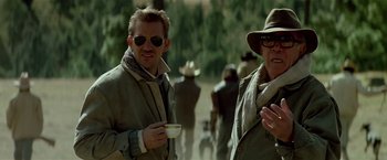 Movie still from “Revenge” (1990), directed by Tony Scott – A man and a woman are standing in a field; Medium shot, Over the shoulder angle