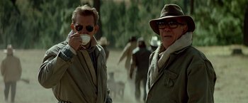 Movie still from “Revenge” (1990), directed by Tony Scott – Two men are standing in the middle of the street; Medium shot, Low angle