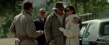 Movie still from “Revenge” (1990), directed by Tony Scott – A man and a woman hugging each other in front of a group of people; Medium shot, Over the shoulder angle