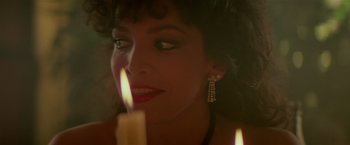 Movie still from “Revenge” (1990), directed by Tony Scott – A beautiful woman with a candle in a dark room; Close Up shot, High angle