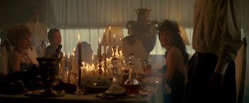 Movie still from “Revenge” (1990), directed by Tony Scott – A woman sitting at a table with a lot of candles; Medium shot, Over the shoulder angle