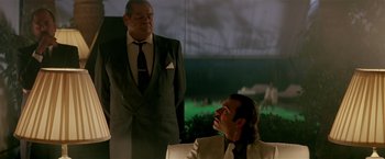 Movie still from “Revenge” (1990), directed by Tony Scott – A man in a suit and tie next to another man in a suit and tie; Medium shot, Low angle