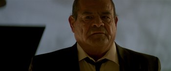 Movie still from “Revenge” (1990), directed by Tony Scott – An older man wearing a suit and tie; Close Up shot, Low angle