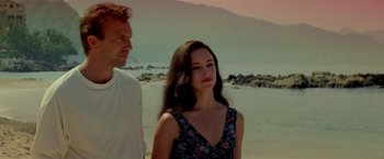 Movie still from “Revenge” (1990), directed by Tony Scott – A man and a woman standing next to each other on the beach; Medium shot, Low angle