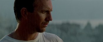 Movie still from “Revenge” (1990), directed by Tony Scott – A man's face in front of a body of water; Close Up shot, Low angle