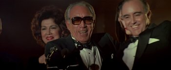 Movie still from “Revenge” (1990), directed by Tony Scott – An older man wearing a tuxedo and a bow tie; Close Up shot, Low angle