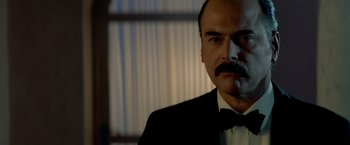 Movie still from “Revenge” (1990), directed by Tony Scott – A person wearing a suit and tie; Close Up shot, Low angle