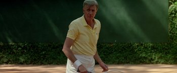 Movie still from “Revenge” (1990), directed by Tony Scott – An older man holding a tennis racquet on a tennis court; Medium shot, Low angle