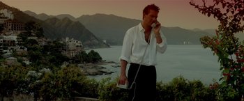 Movie still from “Revenge” (1990), directed by Tony Scott – A man talking on a phone next to a body of water; Medium shot, Low angle