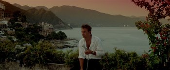 Movie still from “Revenge” (1990), directed by Tony Scott – A man standing on top of a hill next to a body of water; Medium shot, Low angle