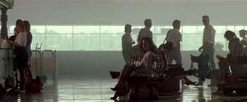 Movie still from “Revenge” (1990), directed by Tony Scott – A woman sitting on top of a suitcase in an airport; Wide shot, Low angle