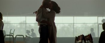 Movie still from “Revenge” (1990), directed by Tony Scott – A man and a woman kissing in front of a window; Wide shot, Low angle
