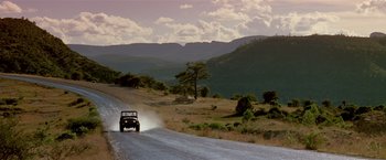 Movie still from “Revenge” (1990), directed by Tony Scott – A jeep driving down a road in the middle of the day; Extreme Wide shot, Low angle