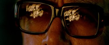 Movie still from “Revenge” (1990), directed by Tony Scott – A man's face wearing a pair of glasses; Extreme Close Up shot, Overhead angle