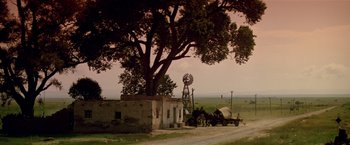 Movie still from “Revenge” (1990), directed by Tony Scott – An old windmill is next to a tree and a building; Extreme Wide shot, Low angle