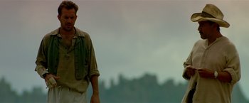 Movie still from “Revenge” (1990), directed by Tony Scott – A man standing on top of a hill with mountains in the background; Medium shot, Low angle