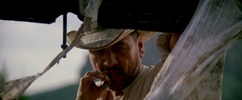Movie still from “Revenge” (1990), directed by Tony Scott – A person wearing a hat smoking a cigarette; Close Up shot, Low angle