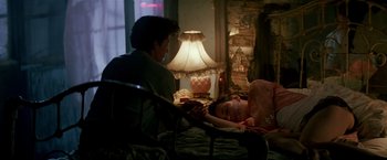 Movie still from “Revenge” (1990), directed by Tony Scott – A young child is laying on a chair with a person sitting next to it; Medium shot, High angle