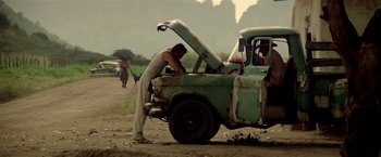 Movie still from “Revenge” (1990), directed by Tony Scott – A man is fixing something in the back of a truck; Wide shot, Low angle