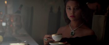 Movie still from “Revenge” (1990), directed by Tony Scott – A woman in a black dress holding a cup of tea; Close Up shot, High angle