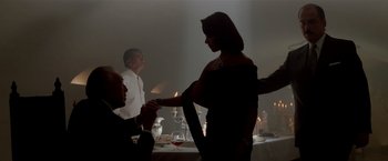 Movie still from “Revenge” (1990), directed by Tony Scott – A man and a woman shaking hands at a dinner table; Medium shot, Over the shoulder angle