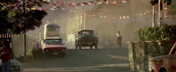 Movie still from “Revenge” (1990), directed by Tony Scott – An old car is driving down the street with a bicycle in the background; Extreme Wide shot, Low angle