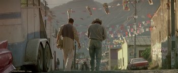 Movie still from “Revenge” (1990), directed by Tony Scott – Two men walking down the street in front of a crowd; Wide shot, Low angle