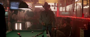 Movie still from “Revenge” (1990), directed by Tony Scott – A man in a cowboy hat standing next to a pool table; Wide shot, Over the shoulder angle