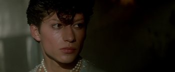 Movie still from “Revenge” (1990), directed by Tony Scott – A person wearing a pearl necklace; Close Up shot, Over the shoulder angle