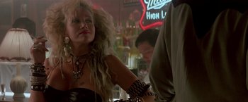 Movie still from “Revenge” (1990), directed by Tony Scott – A woman in a black dress with a cross on her arm; Close Up shot, Over the shoulder angle